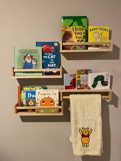 three wooden bookshelves with children's books on them and two towels hanging from the hooks