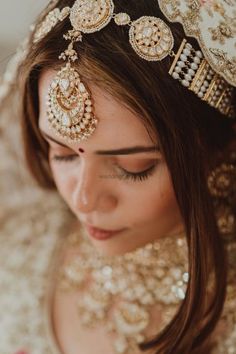 a woman wearing a gold and white bridal headpiece with jewels on her forehead