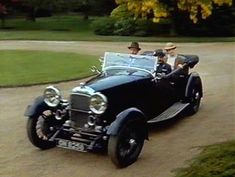 an old fashioned car driving down a road with two men in the back seat and another man standing behind it