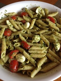 a white bowl filled with pasta covered in pesto and cherry tomatoes, garnished with parsley