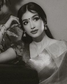 a black and white photo of a woman with long hair in a sari sitting on a couch