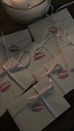 six folded cards with white ribbon and pink lips on them, tied to a table