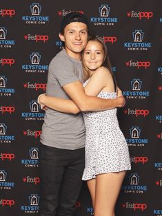 a man and woman hugging each other in front of a backdrop