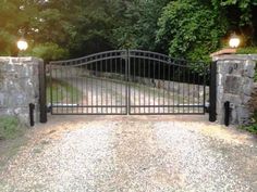 an iron gate with two lights at the top and bottom, leading to a driveway