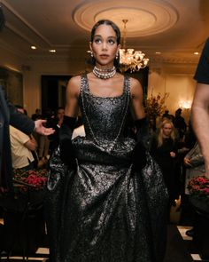 a woman is walking down the runway in a black and silver dress with pearls on her neck