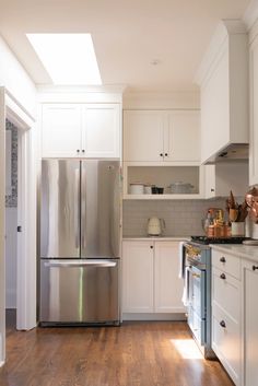 a stainless steel refrigerator in a kitchen with white cabinets and wood flooring on the side