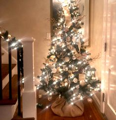 a decorated christmas tree in the corner of a room with stairs and lights on it