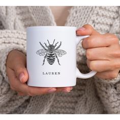 a woman holding a white coffee mug with a bee on it's side and the words lauren written in black