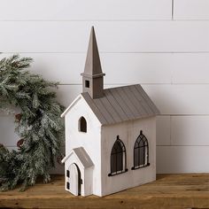 a small white church sitting on top of a wooden table next to a christmas wreath