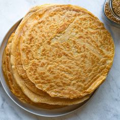 three flat breads on a plate next to a jar of mustard and seasoning