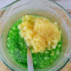 a blender filled with green liquid and yellow substance next to a silver utensil