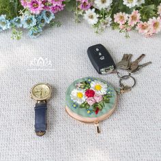 there is a keychain with flowers on it next to a watch and keys