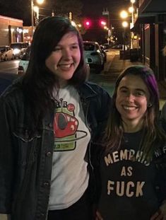 two girls standing next to each other in front of a street at night with traffic lights