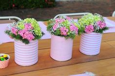 three white vases with pink and green flowers in them on a wooden table outside