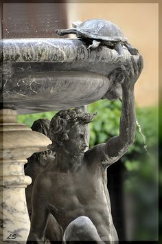 a statue with a turtle sitting on top of it's head next to a fountain