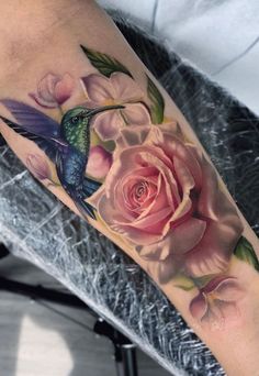 a hummingbird and flower tattoo on the right arm, with pink roses in the background