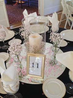 the table is set with white and pink flowers in vases, napkins, and candlesticks