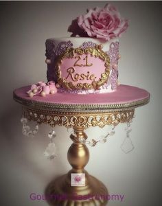 a pink and gold two tiered cake with flowers on the top is sitting on a stand