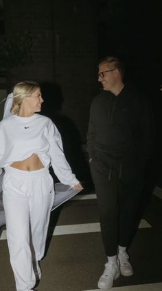 a man and woman walking down the street at night wearing white sweat suits with hoodies