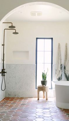 a white bath tub sitting under a window next to a toilet in a room with brick flooring