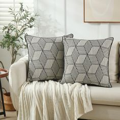 two black and white pillows sitting on top of a couch next to a potted plant