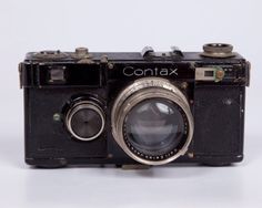 an old camera sitting on top of a white table next to a black object with the word contax written on it