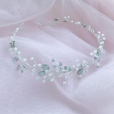 a tiara with white flowers and green leaves on top of a pink fabric background