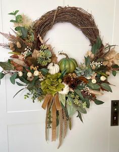 a wreath hanging on the front door decorated with greenery and pumpkins