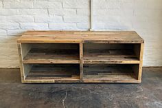 a wooden entertainment center sitting on top of a cement floor next to a white brick wall