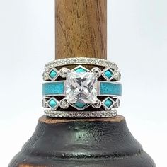 a close up of a ring on top of a wooden stick with diamonds and turquoise stones