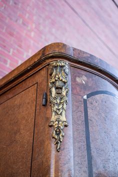 an ornate wooden cabinet with brass decorations on the top and bottom part, in front of a brick wall