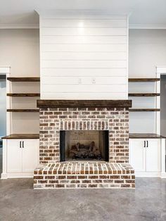 an empty living room with a brick fireplace and white shelving on either side of the fire place