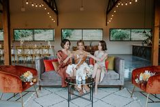 three women sitting on a couch in a living room with red velvet chairs and white rugs