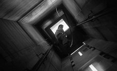 black and white photograph of person sitting on stairs looking out the window at something in the distance