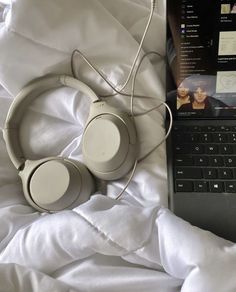 an open laptop computer sitting on top of a bed next to headphones and a white blanket