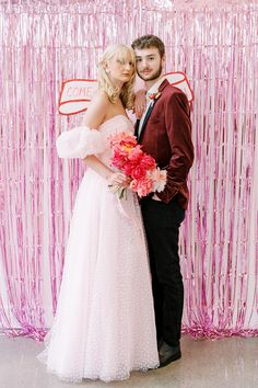 a man and woman standing next to each other in front of a pink backdrop with streamers