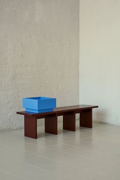 a blue box sitting on top of a wooden bench in front of a white wall