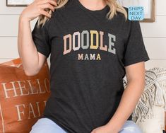 a woman sitting on a couch wearing a t - shirt that says doodle mama