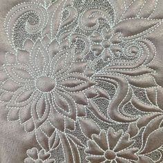 a close up view of an embroidered fabric with white thread and flowers on the side