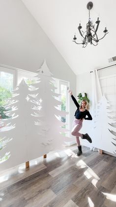 a woman is jumping in the air near a christmas tree cut out of white paper