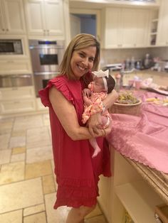 a woman holding a baby in her arms while standing next to a kitchen counter top