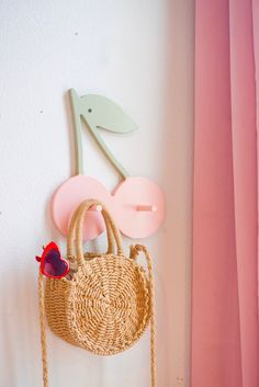 a straw bag hanging on the wall next to a pink curtain and hook with a red heart