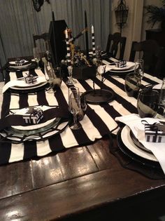 a dining room table set with black and white striped placemats, silverware and candlesticks