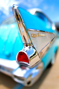 the tail end of an old blue car with its hood up and it's emblem on