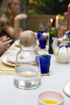 a table topped with plates and bowls filled with food next to bottles of wine on top of a white table cloth