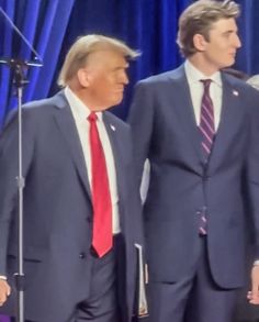 two men in suits and ties standing next to each other with microphones behind them