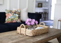 a basket with flowers sitting on top of a wooden table in front of a couch