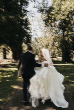 the bride and groom are walking through the park