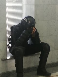 a man sitting on top of a window sill wearing a black suit and helmet