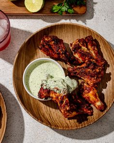 some chicken wings on a wooden plate with dip and lemon wedges next to it